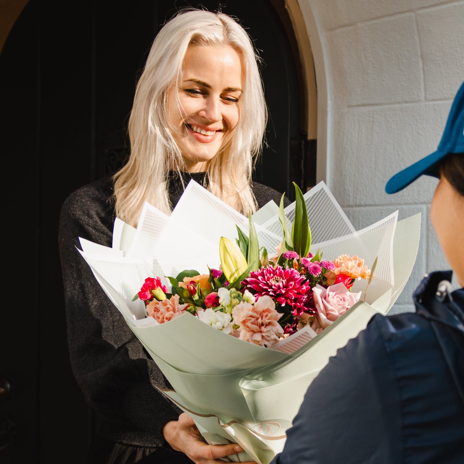 Person receiving a bouquet of flowers from another person outdoors.